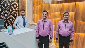 Three men standing in a reception area with a modern design, including a reception desk and a decorative wall. - Hotel Bagga Kuteer (Haridwar)