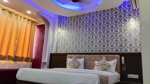A hotel room with a bed, patterned wallpaper, a telephone, and a power outlet. - Hotel Bagga Kuteer (Haridwar)