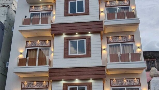 A multi-story building with balconies, decorative wooden trim, and illuminated wall sconces. - Hotel Bagga Kuteer (Haridwar)