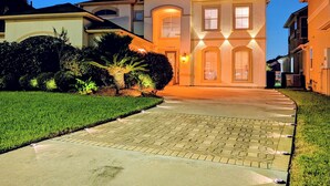 A two-story house with a paved driveway leading to the entrance, surrounded by well-maintained landscaping. - Villa Oak Lake Azure - Ultra Luxury Lakeview Oasis (Houston)
