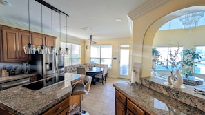 A kitchen with granite countertops, stainless steel appliances, and a dining area with a sofa and chairs. - Villa Oak Lake Azure - Ultra Luxury Lakeview Oasis (Houston)