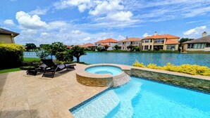 A swimming pool with a hot tub, lounge chairs, and a view of houses across a body of water. - Villa Oak Lake Azure - Ultra Luxury Lakeview Oasis (Houston)