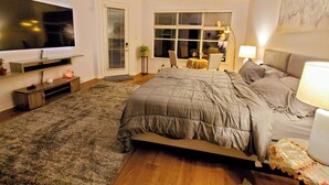 A bedroom with a large bed, a television, a desk with a chair, and a window with blinds. - Villa Oak Lake Azure - Ultra Luxury Lakeview Oasis (Houston)