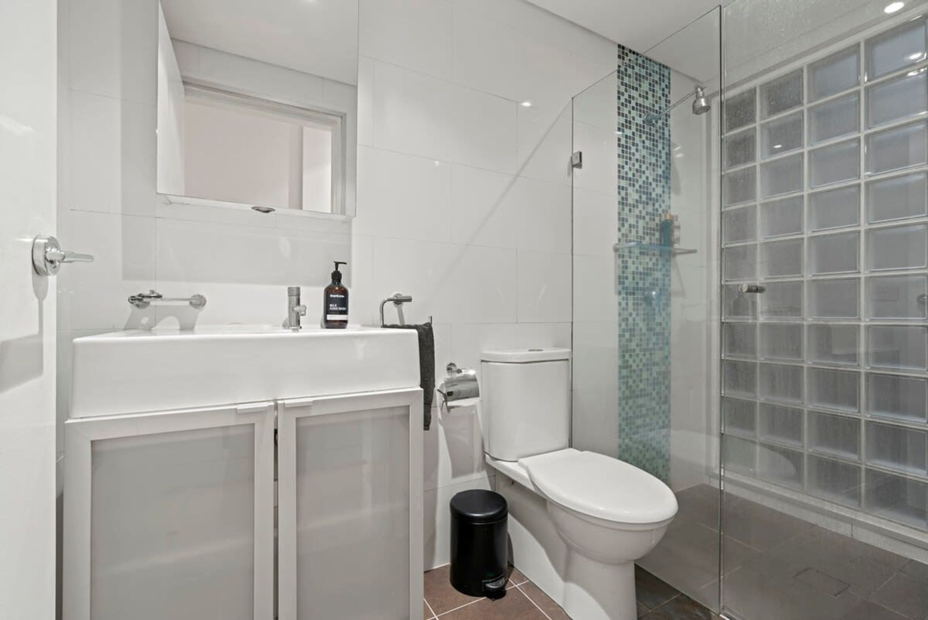 Ein modernes Badezimmer mit Duschkabine aus Glas, einer weißen Toilette und einem Waschbecken mit Spiegel darüber.