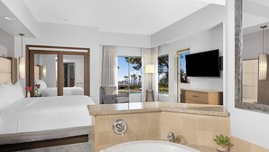Habitación de hotel con una cama grande, baño con bañera, televisión y vistas a palmeras.
