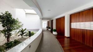 En modern hotellkorridor med en böjd, vit vägg, träpanel och en planteringslåda med gröna växter.