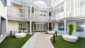 En modern, flervånings atriumgård med konstgjort gräs, vita planteringskärl och en central gångväg.