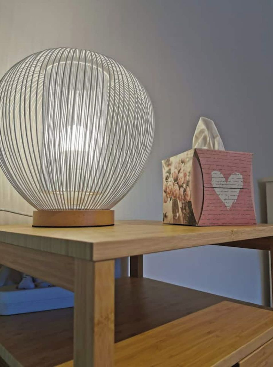 A table with a spherical lamp and a tissue box with a heart design.