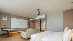 A modern hotel room with a bed, a seating area, a desk, and a large screen displaying the hotel name. - BoYea Hotel (Zhuhai Pingsha Ocean Spring Resort) (Zhuhai)