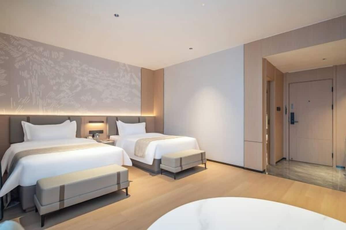 A modern hotel room with two beds, a seating area, and a large wall-mounted screen.