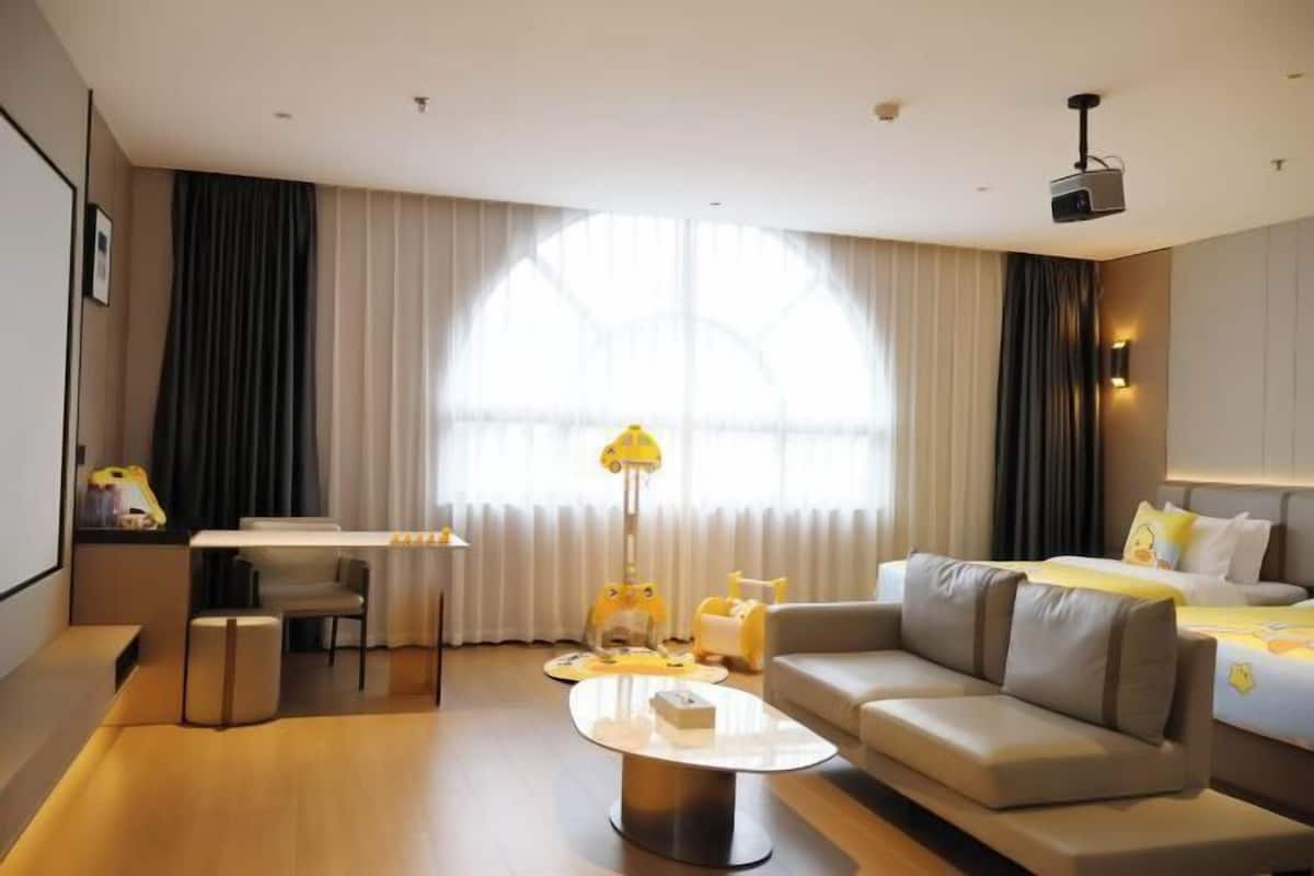 A hotel room with a sofa, a small table, a lamp, a bed, and a projector.