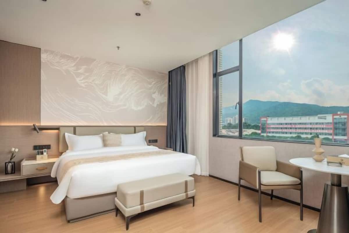 A modern hotel room with a large bed, a desk, and a view of a cityscape.
