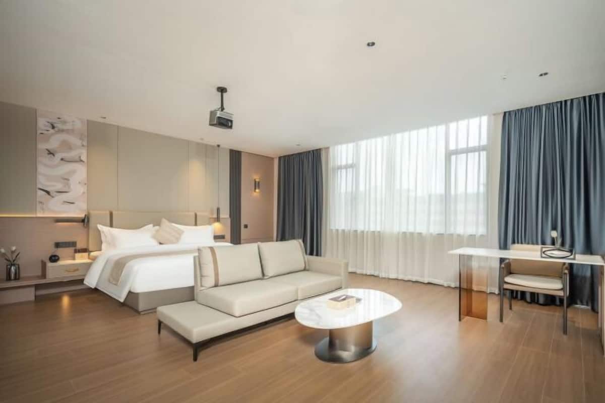 A modern hotel room with a bed, sofa, dining table, and a projector.