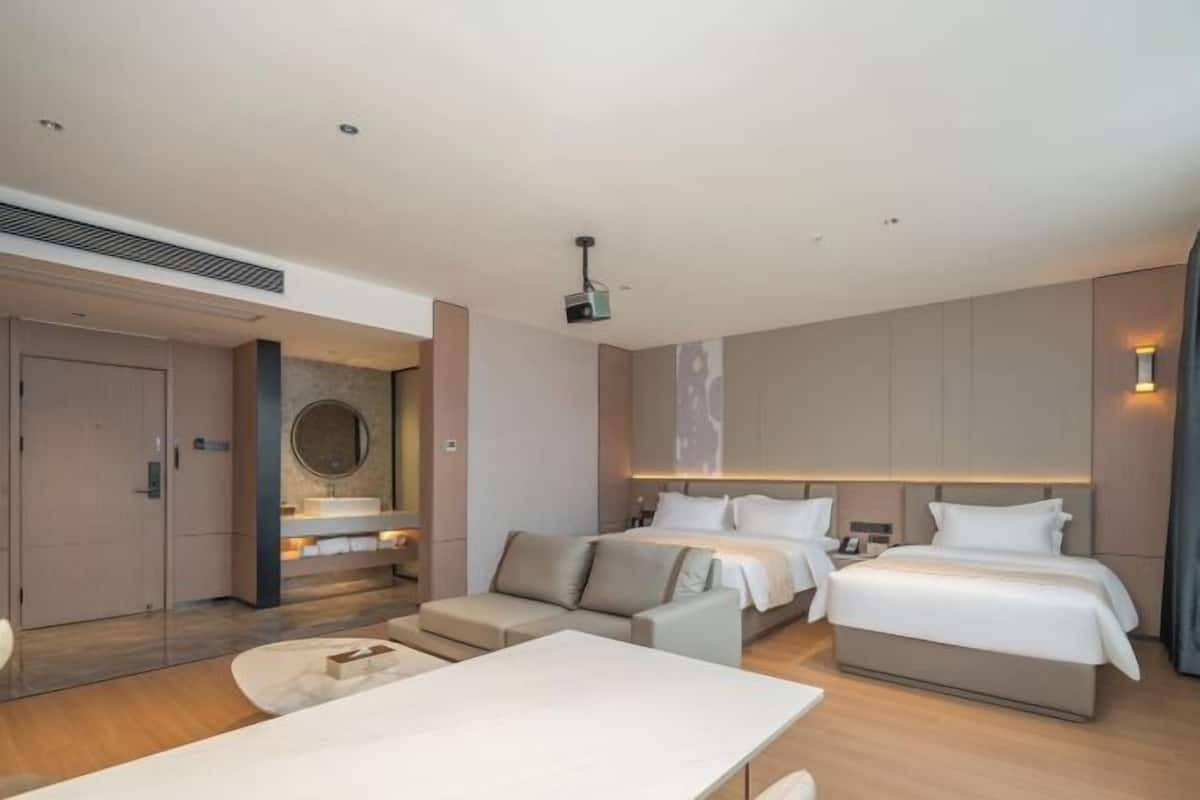 A modern hotel room with a large bed, a sofa, a dining table, and a bathroom with a shower and toilet.