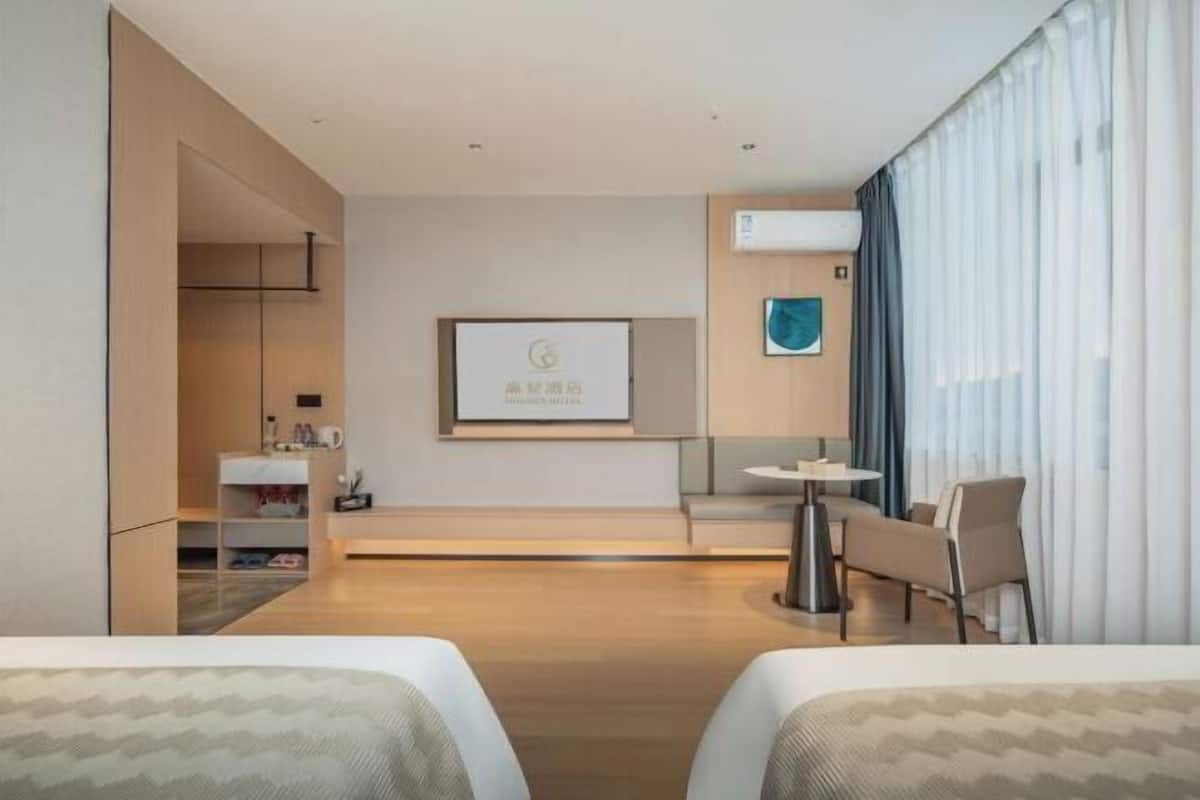 A hotel room with two beds, a desk, a chair, a small table, a sofa, a TV, and a window with curtains.