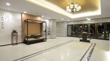A modern hotel lobby with a large seating area, a reception desk, and a large window.