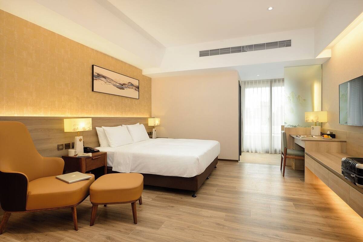Habitación de hotel con cama, escritorio, silla y un pequeño reposapiés.