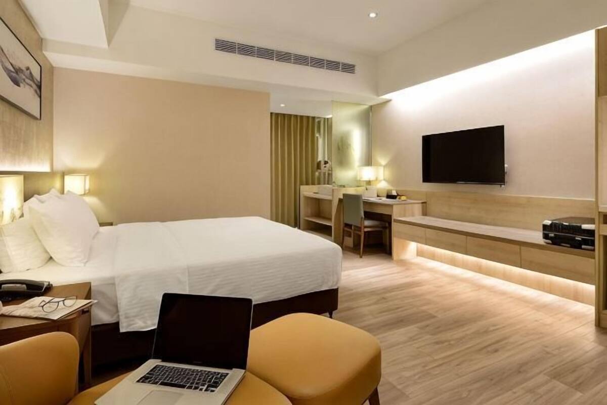 Habitación de hotel con cama, escritorio, silla, ordenador portátil, televisor y espejo.