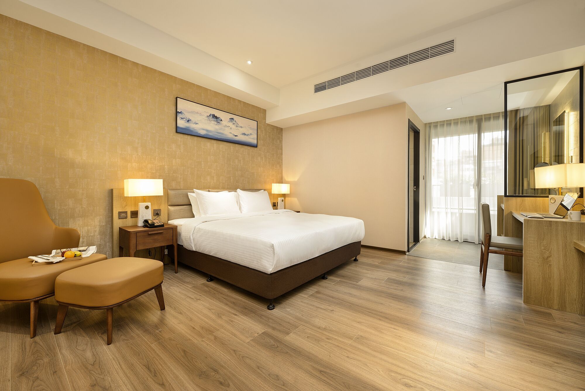 A hotel room with a large bed, two bedside tables with lamps, a chair, a desk with a lamp, and a large window with curtains.
