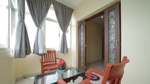 A room with a glass-top table, two wooden chairs, a vase with flowers, and a door with a decorative glass panel. - Nadanam Inn (Puducherry)