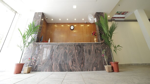A reception area with a marble reception desk, a clock, and potted plants. - Nadanam Inn (Puducherry)