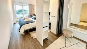 A modern bedroom with a bed, a small stool, a mirror, and a sliding door leading to another room. - The Cliffs - Ria do Vicedo (O Vicedo)