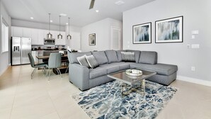 A modern living room with a gray sectional sofa, a glass coffee table, and a blue patterned rug.