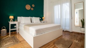 Un dormitorio con una cama, dos mesitas de noche con lámparas, un espejo grande y una ventana con cortinas.