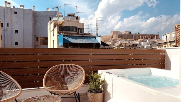 Terraza en la azotea con dos sillones de mimbre, una planta pequeña en maceta y una bañera de hidromasaje.
