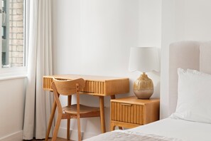A hotel room with a wooden desk, chair, bedside table with a lamp, and a bed with white bedding. - CENTRAL & BRIGHT APARTMENT IN SHOREDITCH  (London)