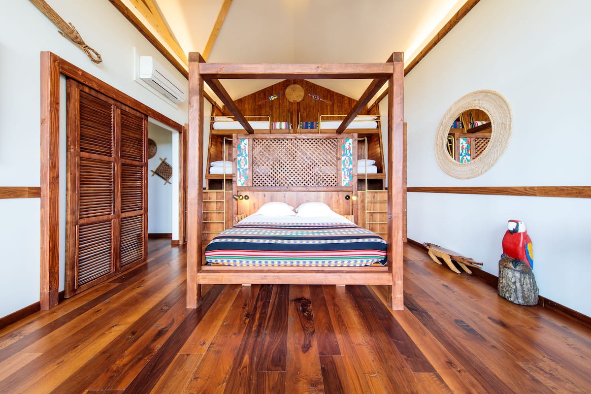 A wooden four-poster bed with a patterned bedspread, a woven wall hanging, and a wooden floor.