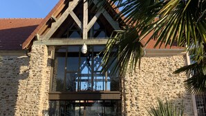 Un edificio de piedra con techo de madera a dos aguas, ventanas de vidrio amplias y una cámara de seguridad.