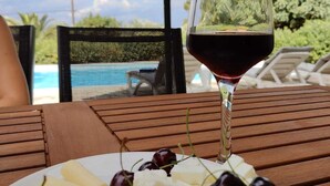 A wooden table with a plate of cheese and cherries, a glass of red wine, and a pool in the background. - Relax with the whole family at this peaceful place to stay. (tzemi)