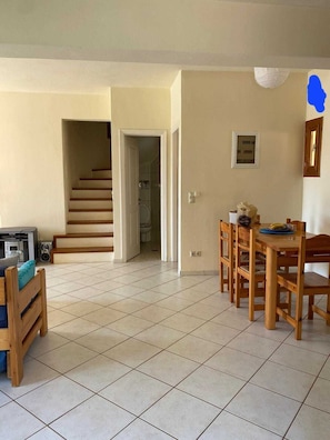A spacious living area with a dining table and chairs, a staircase leading to another room, and a tiled floor.