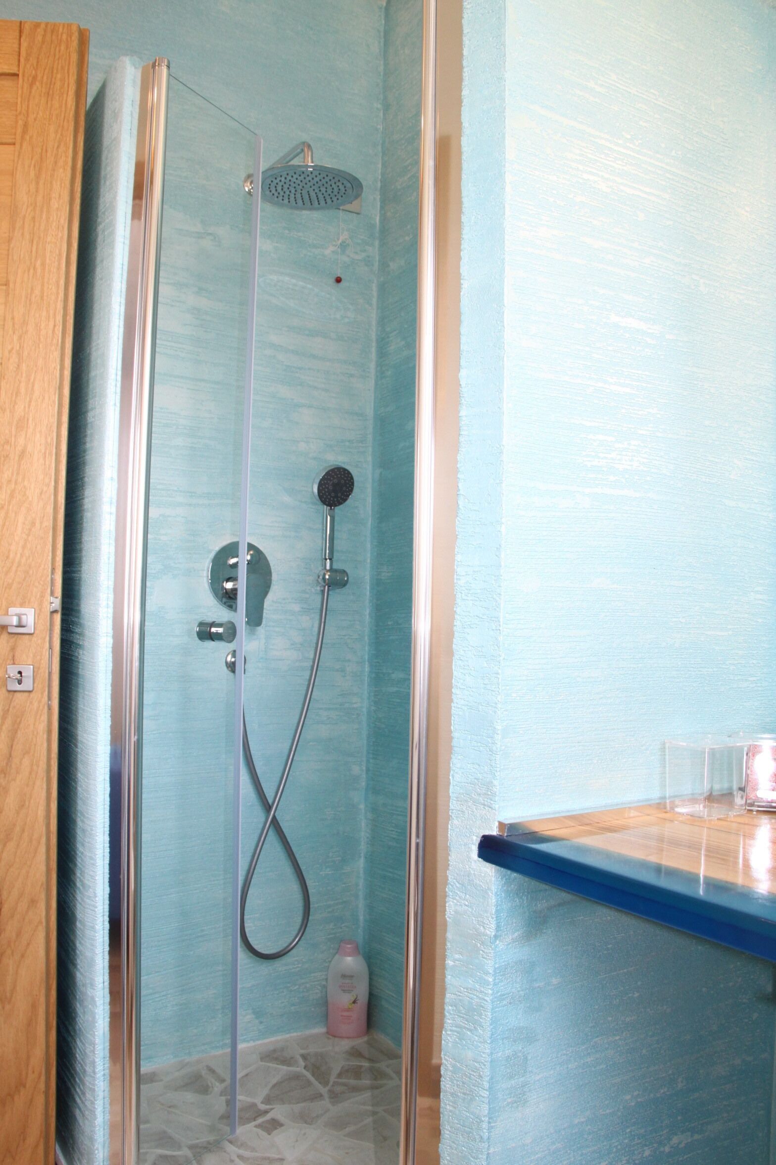A shower with a glass door, a handheld showerhead, and a wall-mounted showerhead.