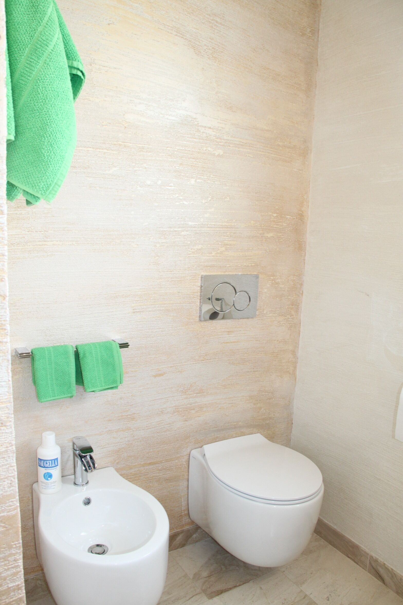A small bathroom with a white sink, two green towels, a toilet, and a bottle of hand soap.