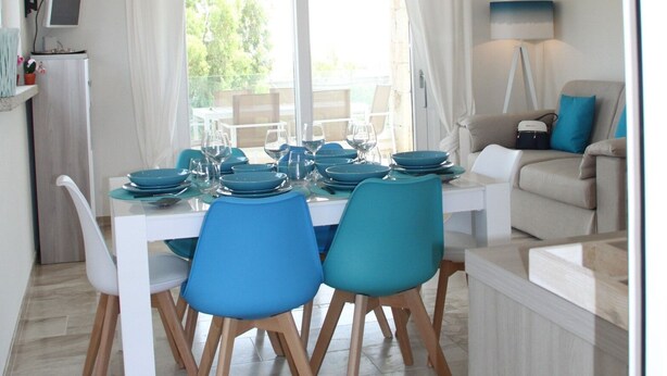 A dining area with a white table set for four, blue chairs, and a ceiling with exposed wooden beams and hanging lights. - R House (Budoni)
