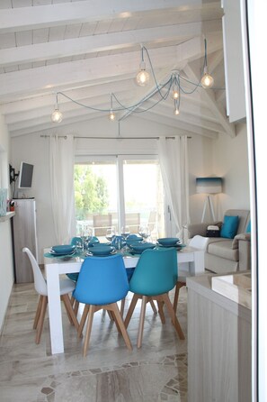 A dining area with a white table set for four, blue chairs, and a ceiling with exposed wooden beams and hanging lights. - R House (Budoni)