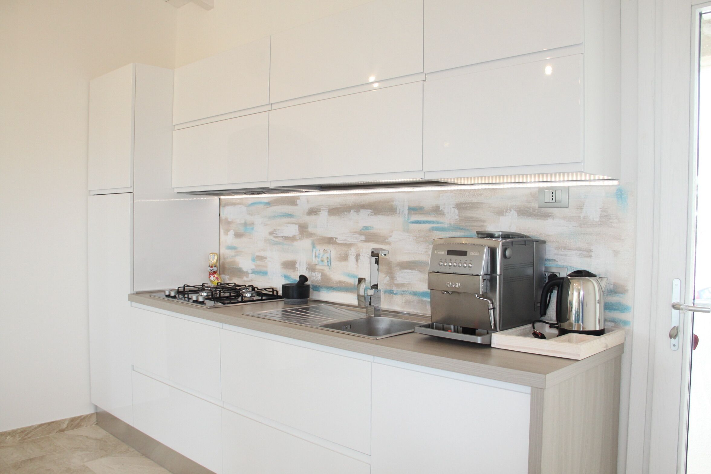 A modern kitchen with white cabinetry, a stainless steel range hood, a coffee machine, and a kettle.
