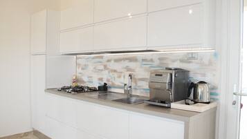 A modern kitchen with white cabinetry, a stainless steel range hood, a coffee machine, and a kettle.