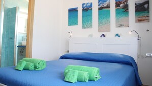 A hotel room with a bed, green towels, a white headboard, and four framed pictures of beaches on the wall. - R House (Budoni)