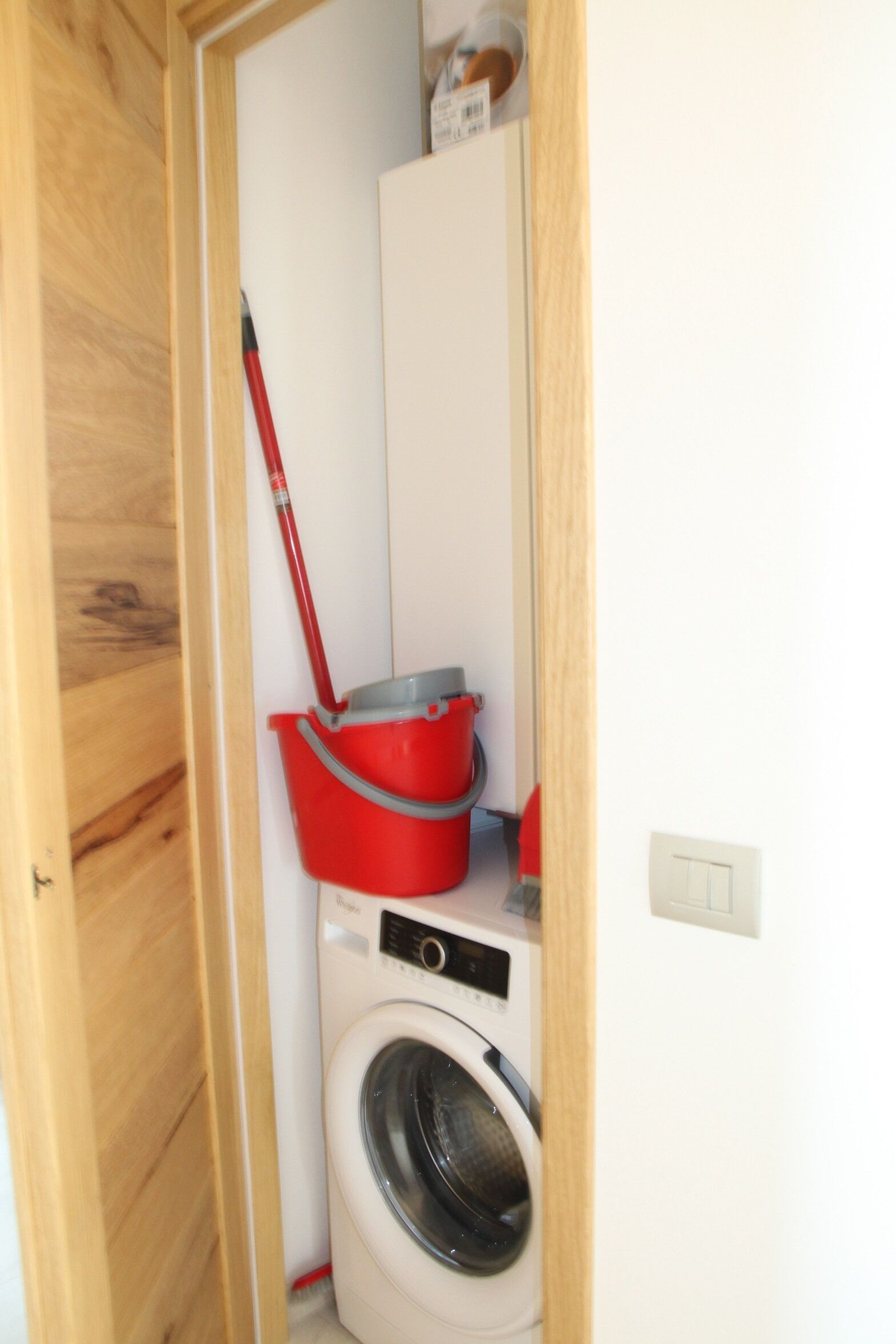 Een wasruimte met een wasmachine, een rode emmer en een dweil.