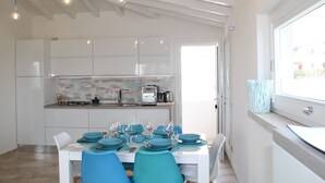 A modern kitchen with white cabinets, a tiled backsplash, and a dining area with a white table set for four. - R House (Budoni)