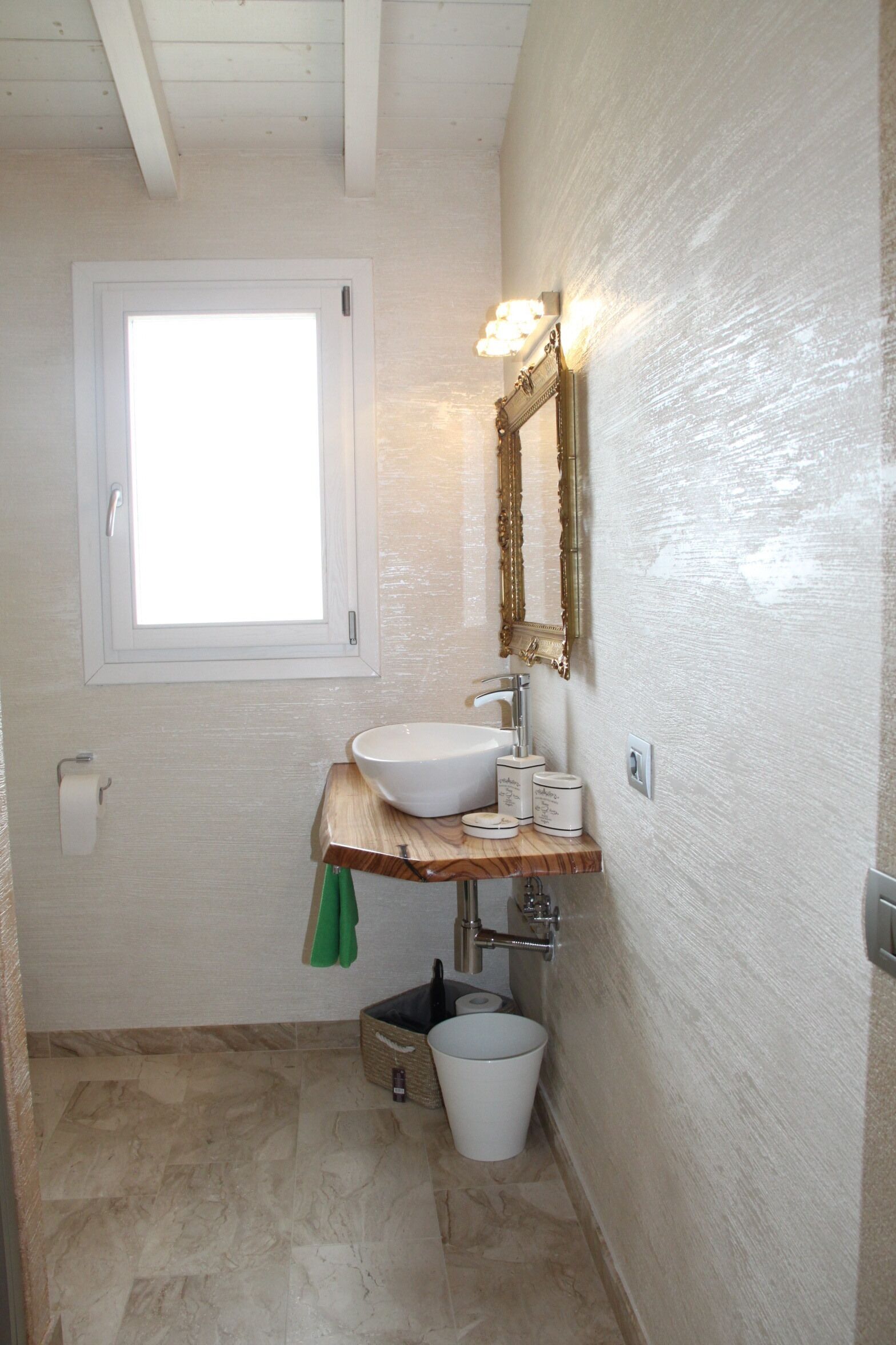 Un baño con un lavamanos blanco, tocador y una ventana sobre el espejo.
