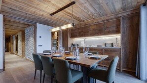 A modern kitchen with wooden cabinets, a dining area with a long table and chairs, and a hallway with wooden floors and walls. - Spacious apartment near slopes with jacuzzi and parking (Montvalezan-La Rosière)