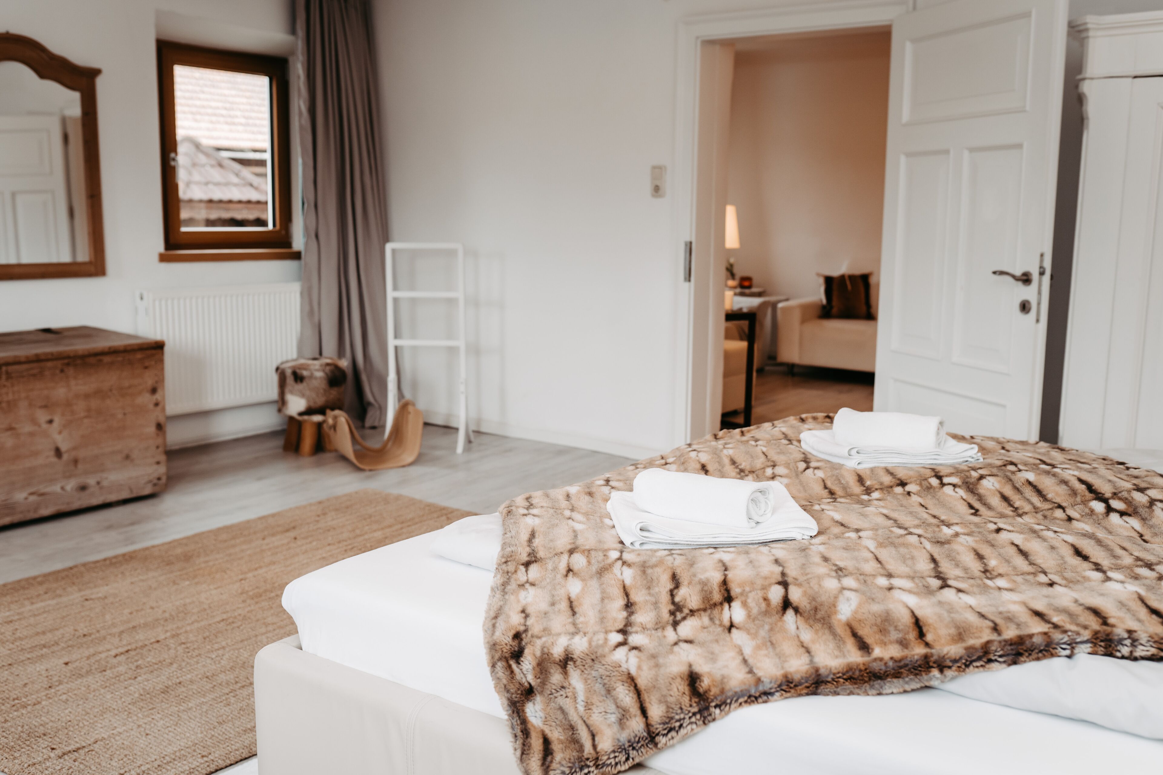A bedroom with a large bed, a wooden dresser, a ladder, and a view of another room through an open door.