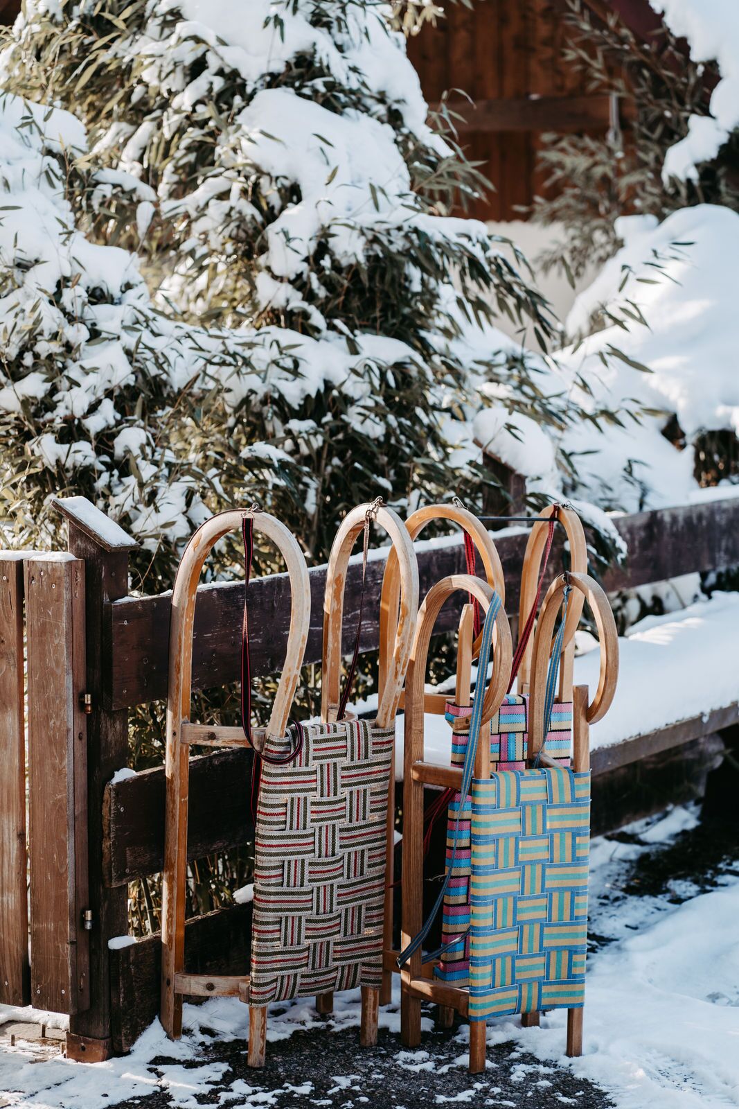 Vier gewebte Taschen mit Holzgriffen, die an einem Holzzaun in einer verschneiten Landschaft lehnen.