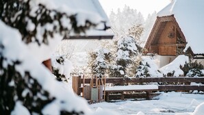 Een houten chalet met een met sneeuw bedekte dak, omgeven door besneeuwde bomen en een houten hek.
