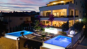 Una moderna casa a due piani con piscina sul tetto e un balcone ben illuminato.