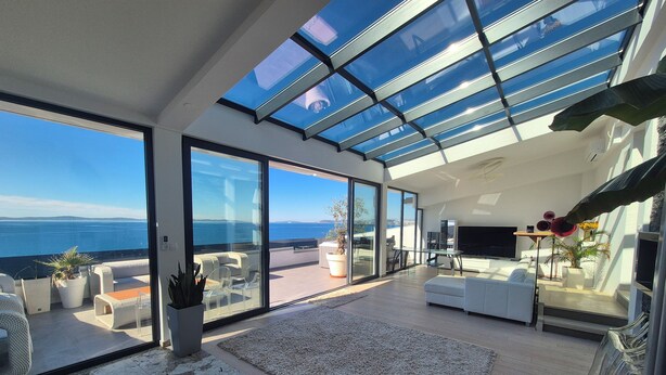 Un soggiorno moderno con un'ampia porta-finestra che si apre su un balcone con vista sul mare.